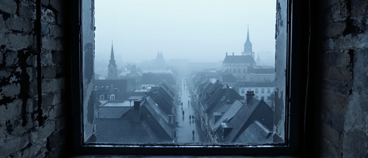 Blick aus einem hohen Fenster über die nebelverhangene Stadt im Morgengrauen, nasse Dächer im Dunst.
