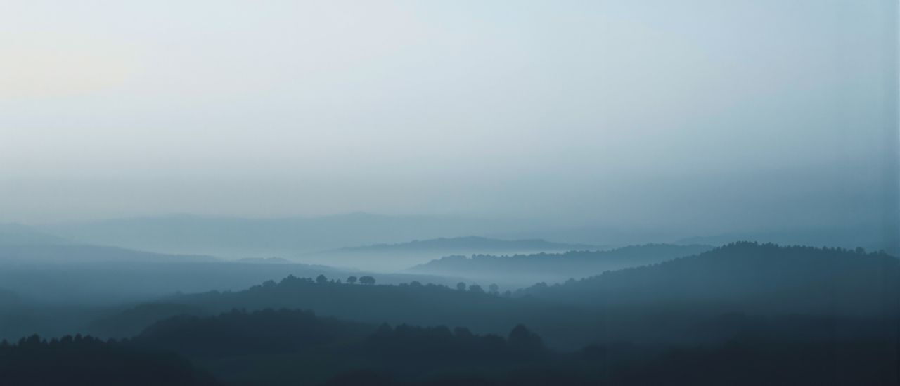 Der Blick aus einem hohen Fenster über eine weite, nebelverhangene Landschaft in mehreren Tiefenschichten.