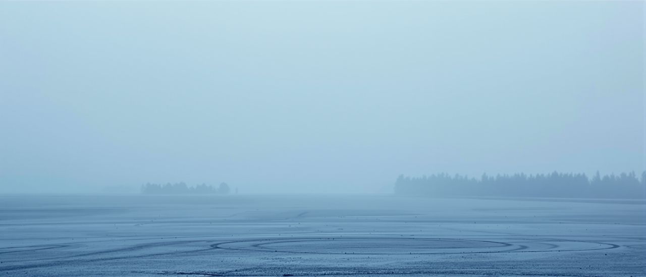 Eine weite, flache Landschaft im Morgennebel, der Horizont verschwindet im Weiß.