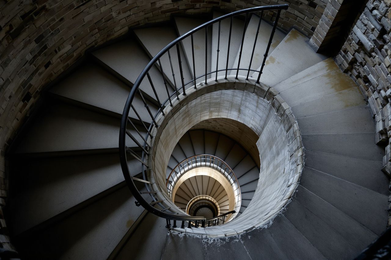 Eine alte Wendeltreppe aus Stein, von unten nach oben fotografiert, kaltes Licht von weit oben.